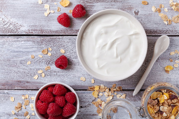 Wall Mural - Greek yogurt in bowl, raspberries and muesli on rustic wooden table top view.