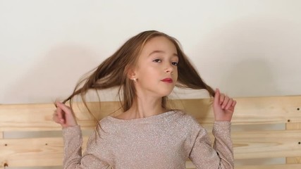 a little cute girl in a shiny jacket sits on a wooden homemade bench in the studio with a white back