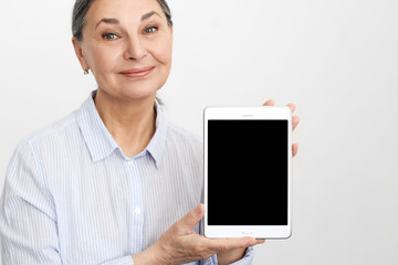 E-commerce, wifi, electronic devices and age concept. Studio image of happy elegant gray haired mature woman using high speed internet connection on digital tablet, showing blank copyspace display