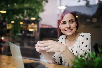 Wall Mural - A portrait of woman with coffee sitting at the table in a cafe, shot through glass.