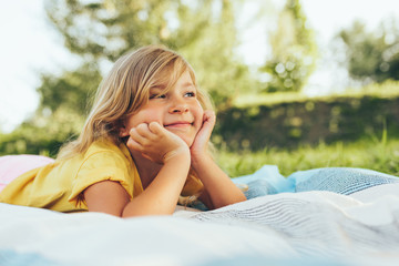 Image of adorable blond little girl playing at nature background. Happy child enjoying summertime in the park. Cheerful kid relaxing in the forest on sunlight outdoors. Happy childhood.