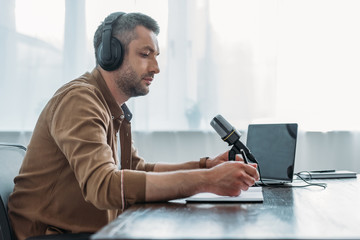 serious radio host in headphones sitting near microphone in broadcasting studio