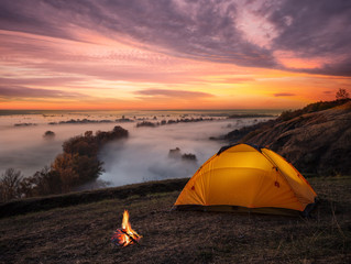 Wall Mural - orange lit inside tent and fire over misty river at sunset