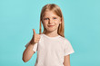© nazarovsergey - Close-up studio shot of a lovely blonde little girl in a white t-shirt posing against a blue background.