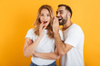 Image of attractive couple man and woman in basic t-shirts whispering secrets or gossips to each other