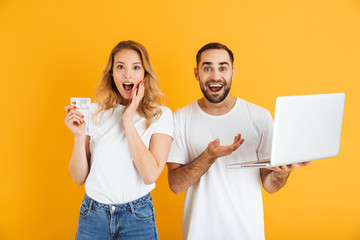 Image of impressed couple man and woman expressing surprise together while holding laptop and credit card