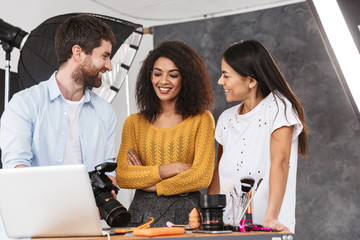 Wall Mural - Portrait of pleased multiethnic people looking at laptop while photo shooting with professional camera in studio