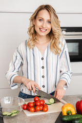 Happy young beautiful woman posing at the kitchen at home cooking.