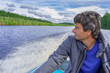 © Tatyana_Andreyeva - Handsome middle-aged man sitting at boat stern, floating along northern river and relaxing on beautiful landscape background in summer day. Travel concept. Chernaya river, Karelia, Russia
