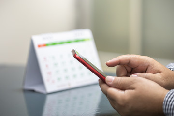 People Communination and technology concept. Close up of man hand holding, touch and using mobile smartphone and desktop calendar as background.