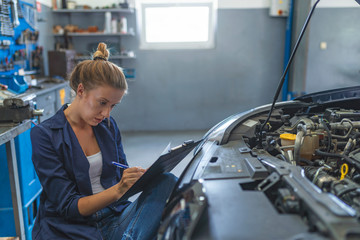 Wall Mural - Cheerful female car technician enjoying working at the garage, copy space. Repair, car service concept Auto car repair service center. Female auto mechanic