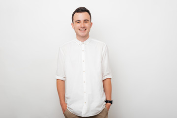 Wall Mural - Portrait of a young smiling guy who is holding his hands in his pants pockets on white background.