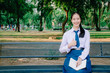 © TeTe Song - Lovely teenage girl wearing school uniform reading book and thumbs up sitting on a bench at the park.