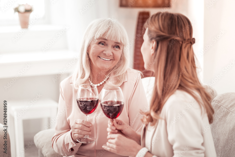 Blond elderly smiling woman having a glass of wine with her daughter ...