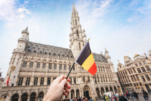 Woman Tourist Holds In Her Hand A Flag Of Belgium Against The Background Of The Grand-Place Square In Brussels, Belgium