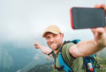 Wall Mural - young backpacker man taking selfie picture using smartphone and showing thumbs up during walking by 