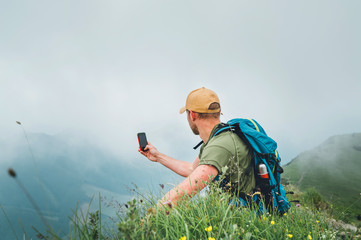 Wall Mural - young backpacker man taking picture of cloudy valley bottom using smartphone during walking by the f