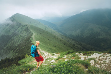 Wall Mural - backpacker hiker man walking by the foggy cloudy weather mountain range path with backpack. active s