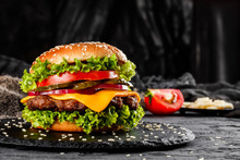 Beef Burger With Cheese, Tomatoes, Red Onions, Cucumber And Lettuce On Black Slate Over Dark Background. Unhealthy Food