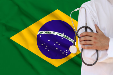 male doctor in white coat holding in his hand a medical instrument with a stethoscope against the background of the national flag, close-up, concept, copy space