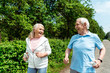© LIGHTFIELD STUDIOS - cheerful woman with grey hair looking at husband while holding bottle and running in park