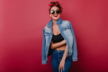 Pleased Girl Wears Jeans Laughing On Claret Background. Spectacular Female Model Looking To Camera Through Black Sunglasses.