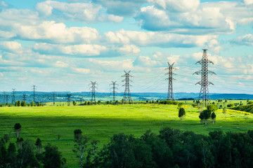 High voltage transmission towers on green grassland at sunny summer day  