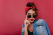 Adorable pensive girl in sunglasses posing on claret background. Graceful black-haired female model in vintage attire thinking about something.