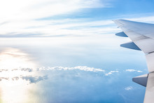White Airplane In Blue Sky With View From Window High Angle During Sunny Day With Plane Wing And Sun Setting Above Horizon With Light Path