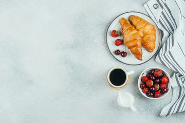 Wall Mural - Delicious breakfast food concept. Coffee, croissants, strawberry and cherry for breakfast on light concrete background. Top view with copy space