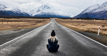 Girl With Blonde Hair Wearing A Hat Sits In The Middle Of The Road In New Zealand Looking At The Mountain View
