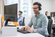 © Bojan - Smiling handsome male customer support phone operator with headset working in call centre. Group of sales agent working in office.