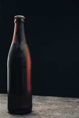 Aufkleber - Close up Glass brown Bottle of beer on a dark wooden table and black background behaid.