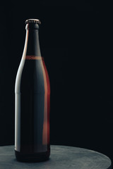 Poster - Glass brown Bottle of beer on a dark round wooden table and black background behaid.