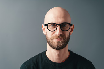 Young smiling man with beard and glasses on gray studio background