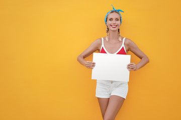 Your text here. Colorful studio portrait of pretty young woman showing empty blank board with copy space against yellow wall.