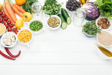 top view of organic fruits and vegetables near glass jars on wooden white table with copy space