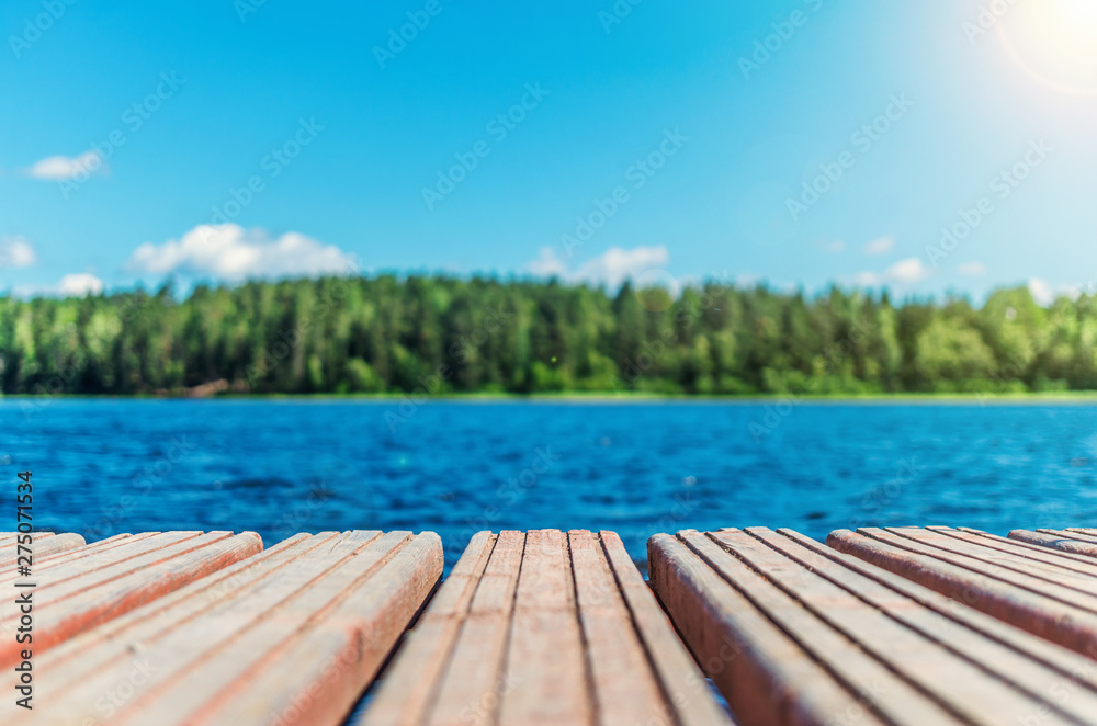 Wooden timber of a rural mooring on a lake in the middle of the forest. A peaceful river dock in the woods.Sunny footbridge. Minimal background with blue sky,clean lake and mooring in the country side - obrazy, fototapety, plakaty 