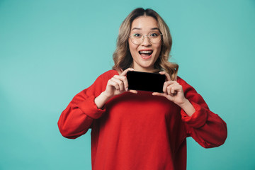 Happy young woman posing isolated over blue wall background showing display of mobile phone.