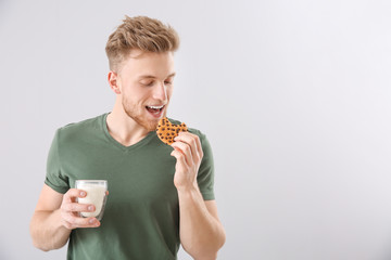 Wall Mural - Handsome young man with tasty cookie and glass of milk on light background