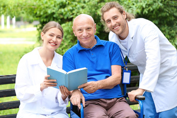 Poster - Elderly man with caregivers reading book in park