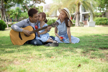 Wall Mural - Happy Asian family. Father, mother and daughter  in kissing at a park at natural sunlight background. Family vacation concept.