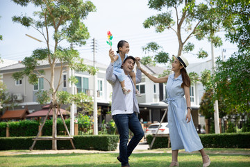 Wall Mural - Happy Asian family. Father gave his daughter a piggyback at a park at natural sunlight background and house. Family vacation concept with copy space