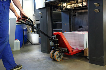 Printing house. The employee loads the paper into the printing machine.