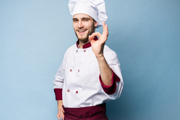 Wall Mural - Positive professional happy man chef showing tasty ok sign isolated on light blue.