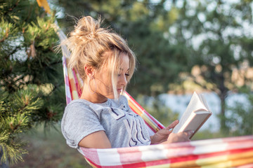 Canvas Print - young attractive caucasian woman reading book in hammock in the forest, lake on the background