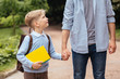 © Iryna - Parent take child to school. Pupil of primary school go study with backpack outdoors. Father and son go hand in hand. Beginning of lessons. Back to school. First day of fall. Elementary student.