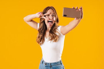 Image closeup of excited caucasian woman wearing basic t-shirt showing peace sign while taking selfie photo on cellphone