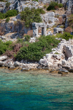 An Ancient City Ruins Stand Near The Clear Green Water Between Rocks And Green Grasses