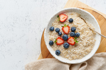 Wall Mural - Oatmeal porridge rustic with berries, dash diet, on white wooden background top view